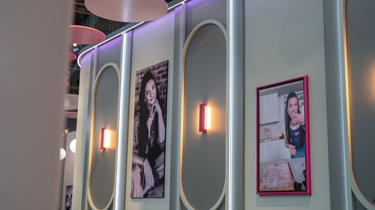 A mint-green wall featuring two portraits of food creator Saliha ‘Sally’ Özcan in Sallys Café in the Icelandic themed area of Europa-Park. The portrait on the left is in black and white. In the portrait on the right, Sally is standing in her baking outfit in her studio kitchen, tasting a slice of cake straight from the baking tray.