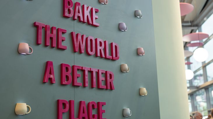 A mint-green wall in Sallys Café in the Icelandic themed area of Europa-Park, decorated with lots of colourful cup-shaped lamps. In the centre is the slogan 'Bake the world a better place' in pink.