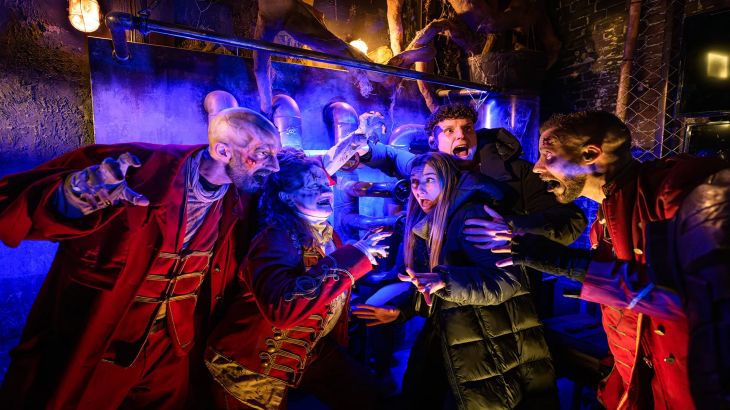Three Traumatica performers wearing red capes scare two visitors.