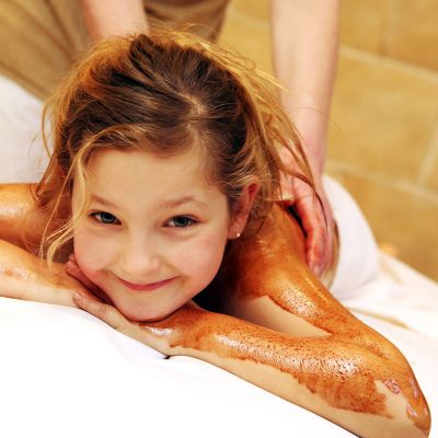 Kind auf der Liege mit Schokoladen-Peeling an den Armen