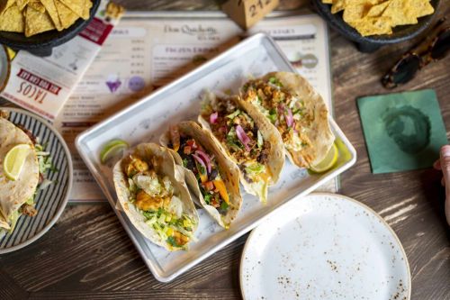 Four freshly prepared Mexican-style tacos with fresh ingredients, served on a table with crispy nachos.