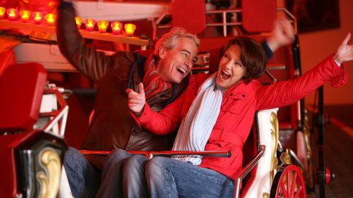 Zwei Personen lachen und heben ihre Hände während der Fahrt mit der Attraktion Feria Swing.