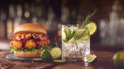 Gin Tonic Glas mit Limetten und Thymian. Daneben ist ein Burger zu sehen.
