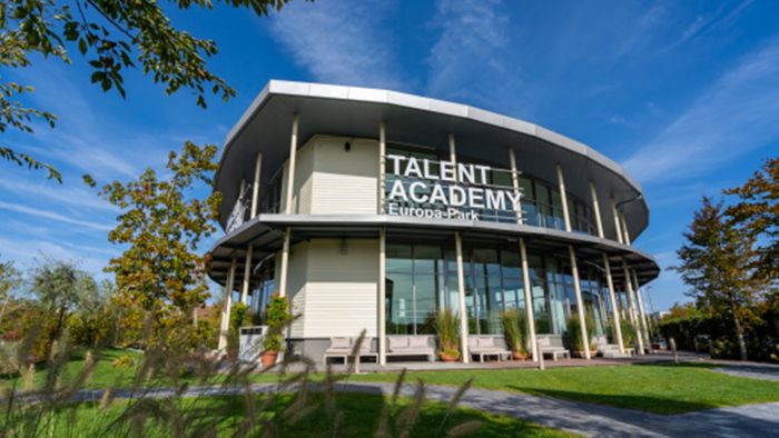Die TALENT ACADEMY des Europa-Park von außen bei blauem Himmel und von grüner Landschaft umgeben.