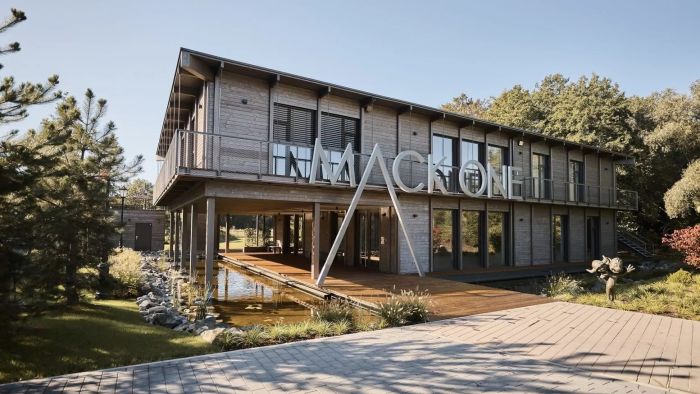 Der moderne MACK One-Standort in Frankreich im Industrial-Stil, mit Holzfassade und großen Fensterfronten, ist von vielen grünen Bäumen umgeben.