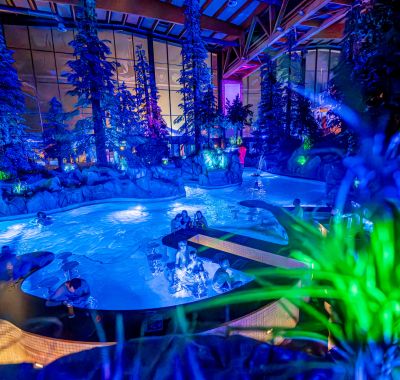 Paar im Wellenbad des Surf Fjords, der Mann trägt seine Freundin auf dem Rücken