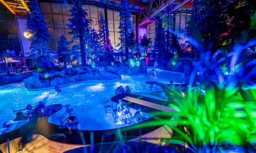 Paar im Wellenbad des Surf Fjords, der Mann trägt seine Freundin auf dem Rücken