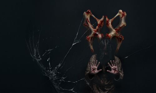 Traumatica character water corpse with an ‘X’ carved into both palms stands in front of bloody bones.