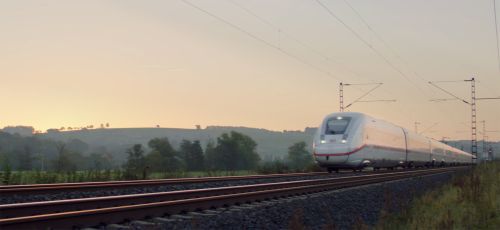 Zug der Deutschen Bahn fährt im Morgengrauen an einem Wald vorbei.